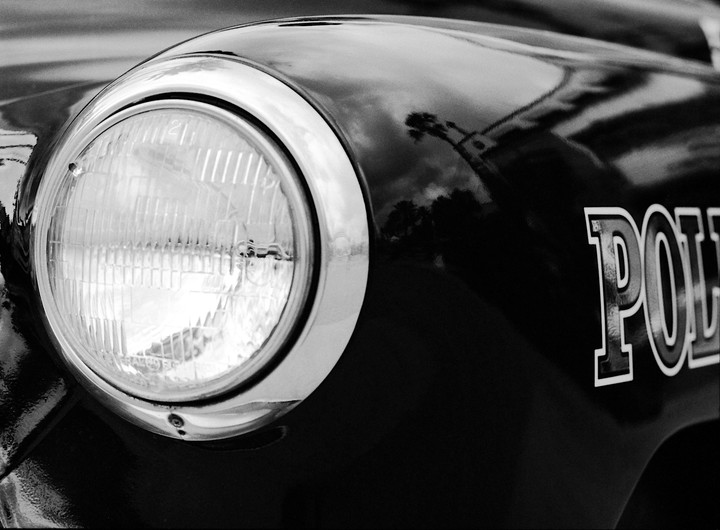 A close-up of a police car headlight and the word "POLICE" on the side of the vehicle.