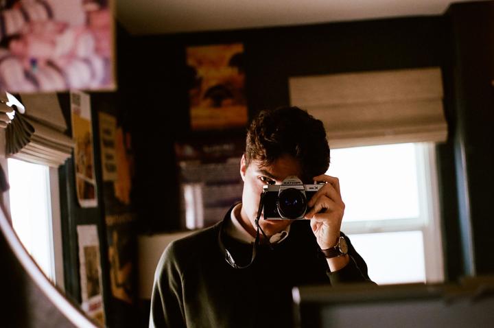 A man takes a self-portrait in a mirror, holding a camera to his face.