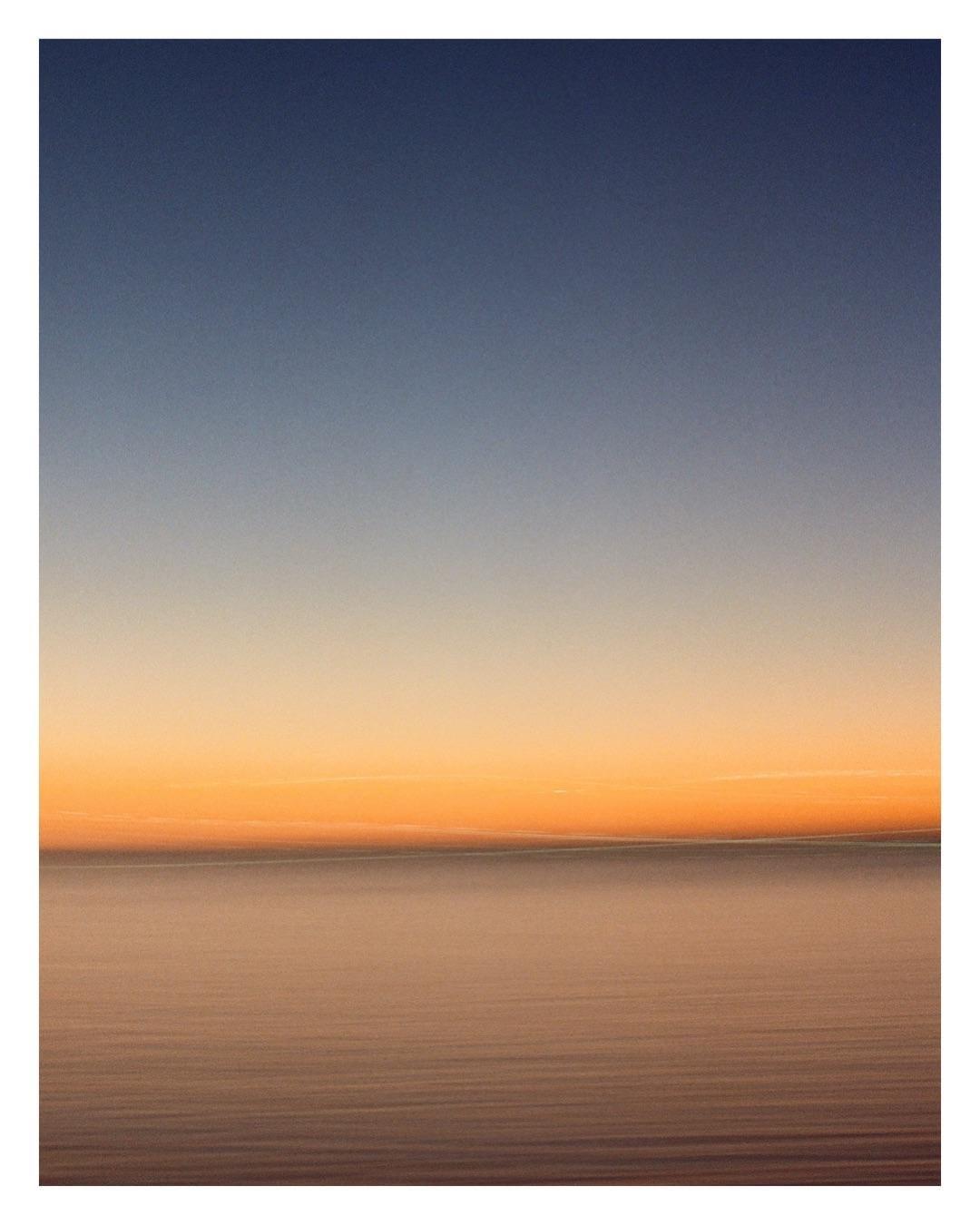 The horizon separates a dark blue sky from a body of water reflecting the orange glow of the sunset.