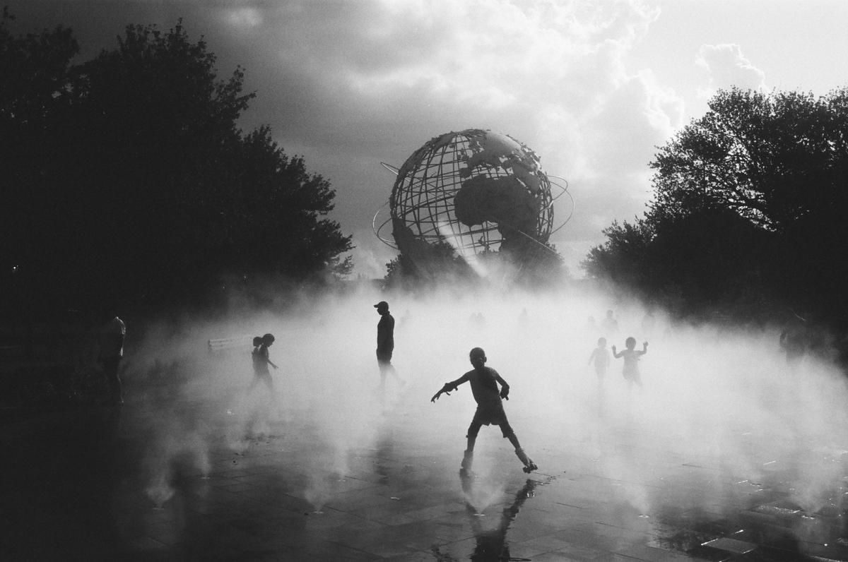 Children play in a misty fountain with the Unisphere in the background.