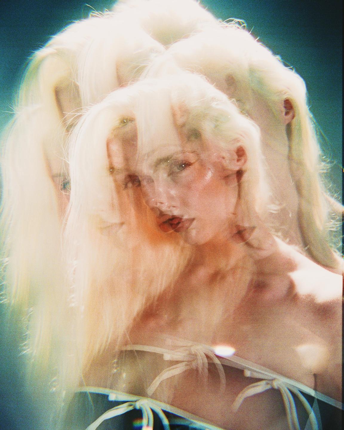 A woman with long blonde hair is depicted in a multiple exposure portrait with a blue background.