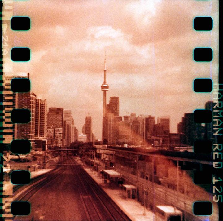 A cityscape with a prominent tower and numerous buildings is seen from above a train track and station.