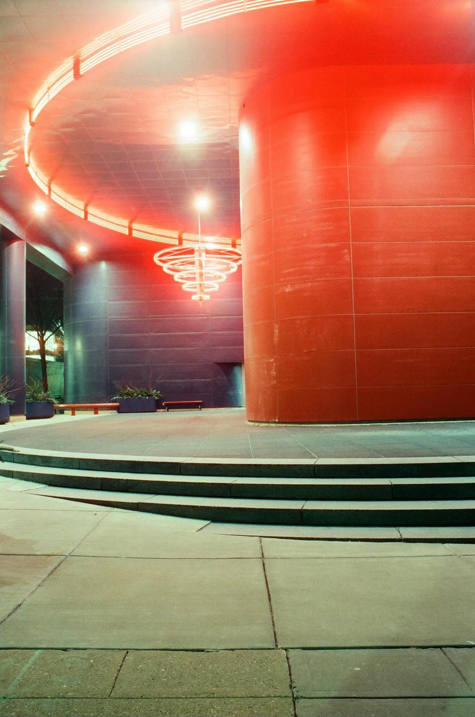 A modern building with a large red column and red neon lighting on the ceiling is illuminated at night.