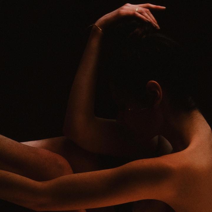 A woman is curled up with her arms around her legs, illuminated by warm light from the side.
