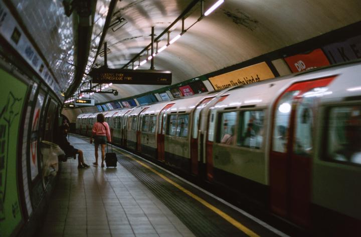 A woman with a suitcase stands on a subway platform as a train pulls into the station.