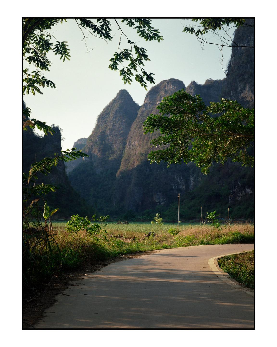 A winding road leads through a valley with towering karst mountains under a clear sky.