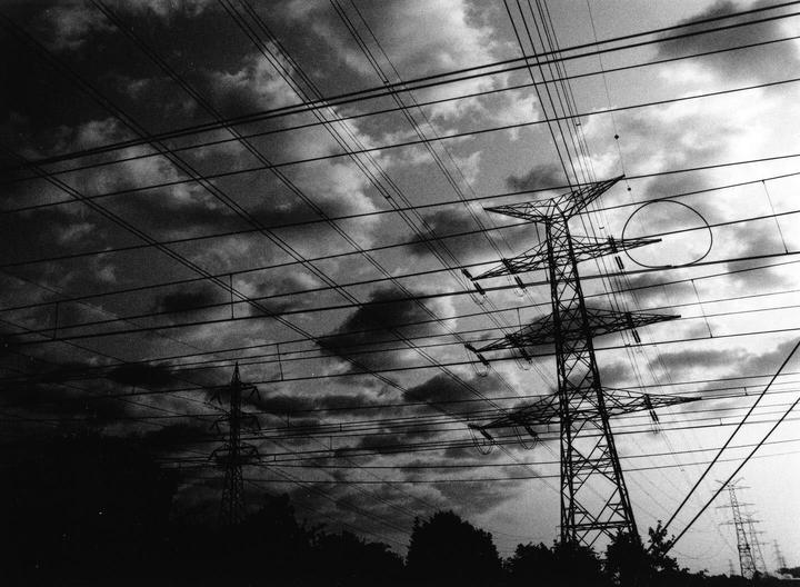 A low-angle view shows multiple power lines and transmission towers against a cloudy sky.