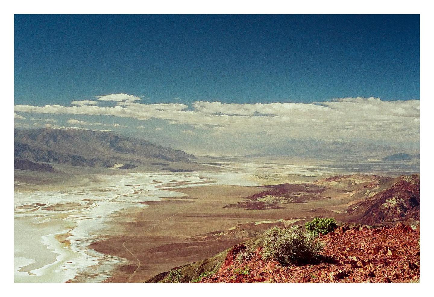 A vast desert landscape with mountains and a salt flat is visible under a blue sky with clouds.