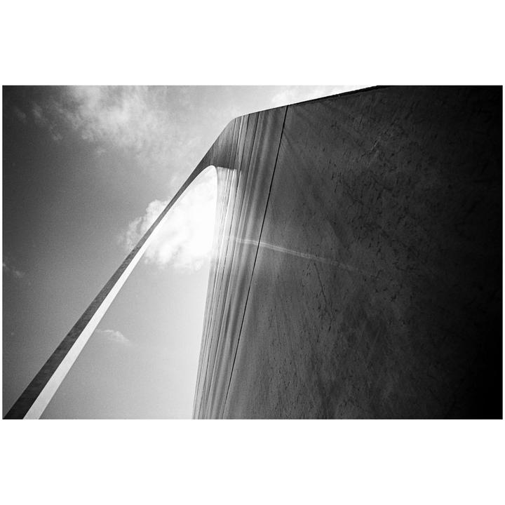 The Gateway Arch is visible from a low angle, with sunlight flaring from behind it.