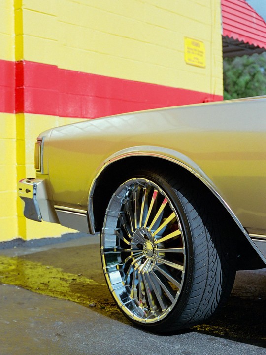 A gold car with chrome rims is parked next to a yellow and red building.