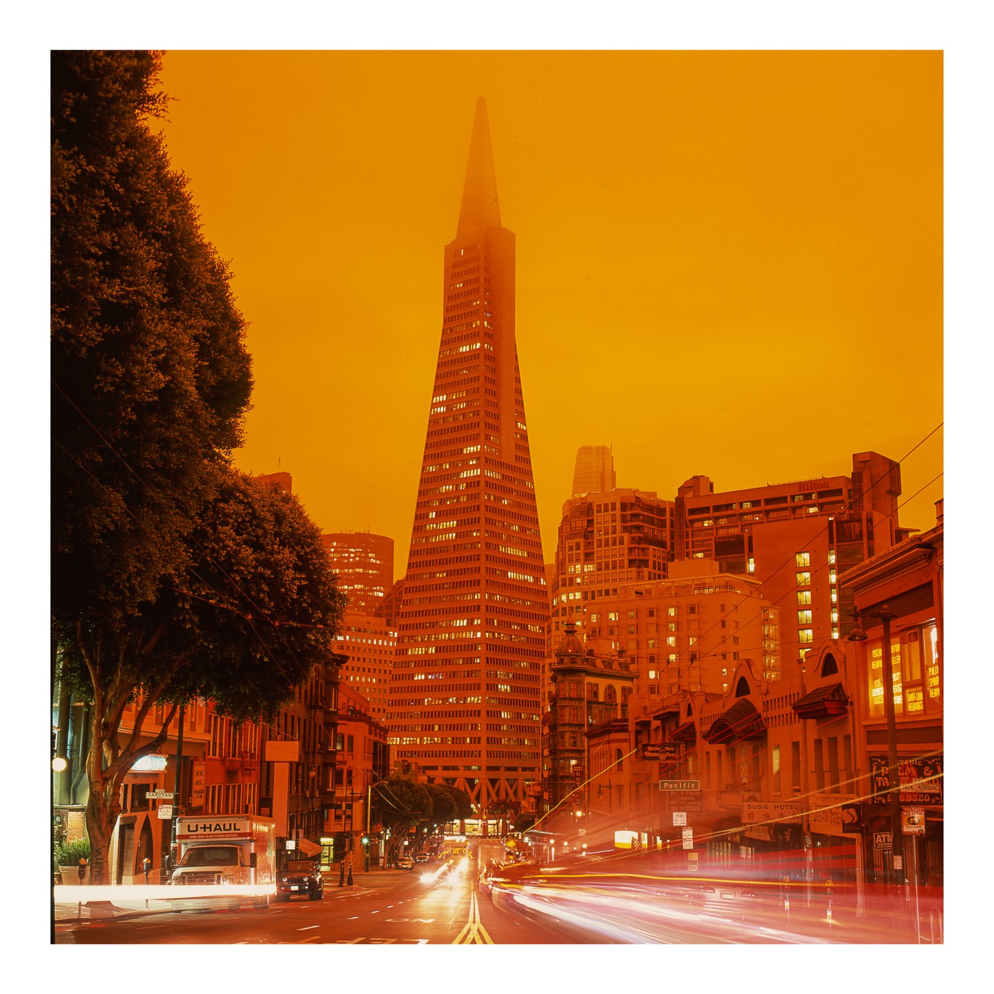 A street in San Francisco is filled with orange light and car light trails, with the Transamerica Pyramid in the background.