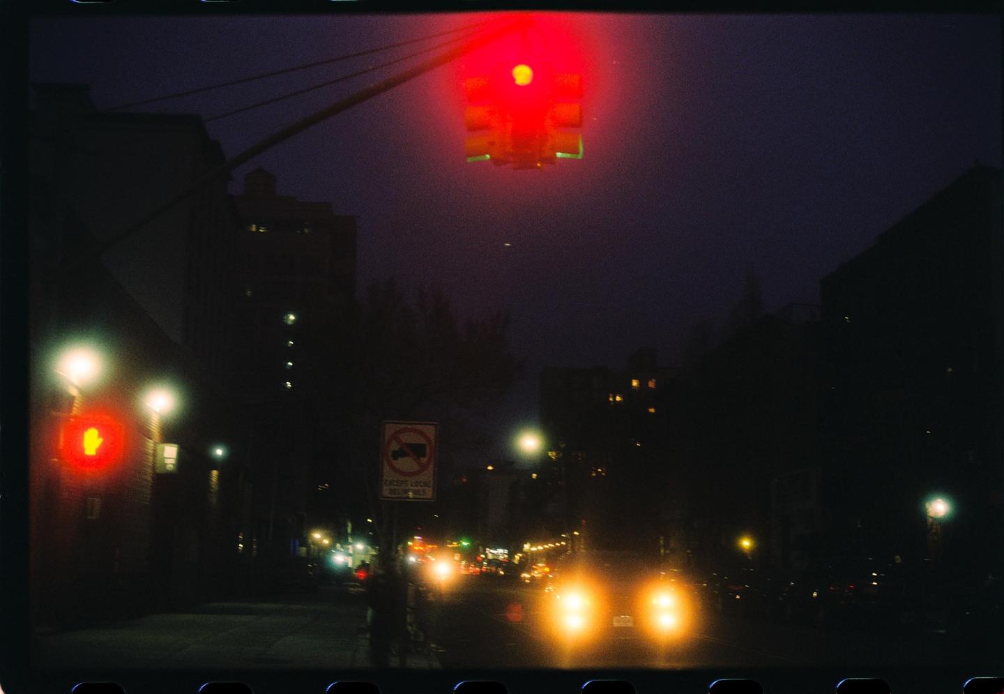 A red traffic light hangs over a street at night with car headlights visible in the distance.
