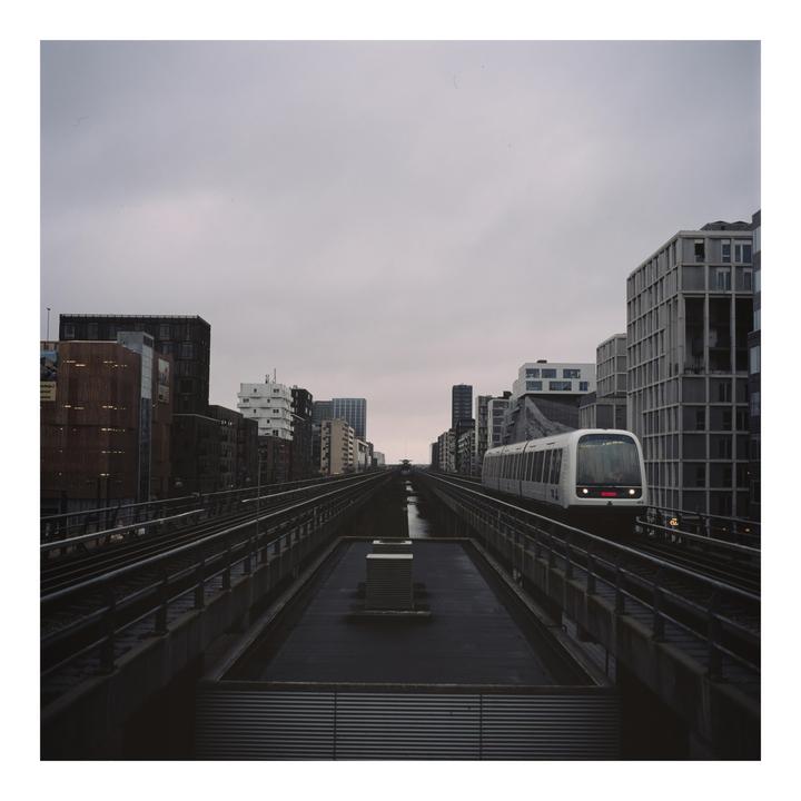 A train travels on an elevated track through a city with tall buildings under a cloudy sky.