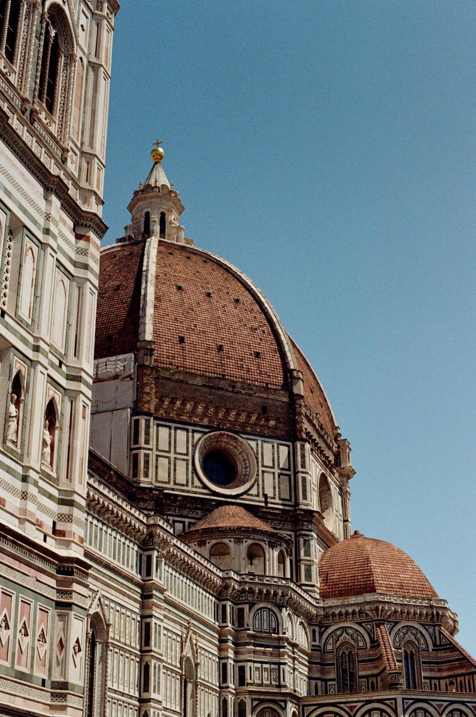 A large domed cathedral with intricate architectural details stands against a clear blue sky.