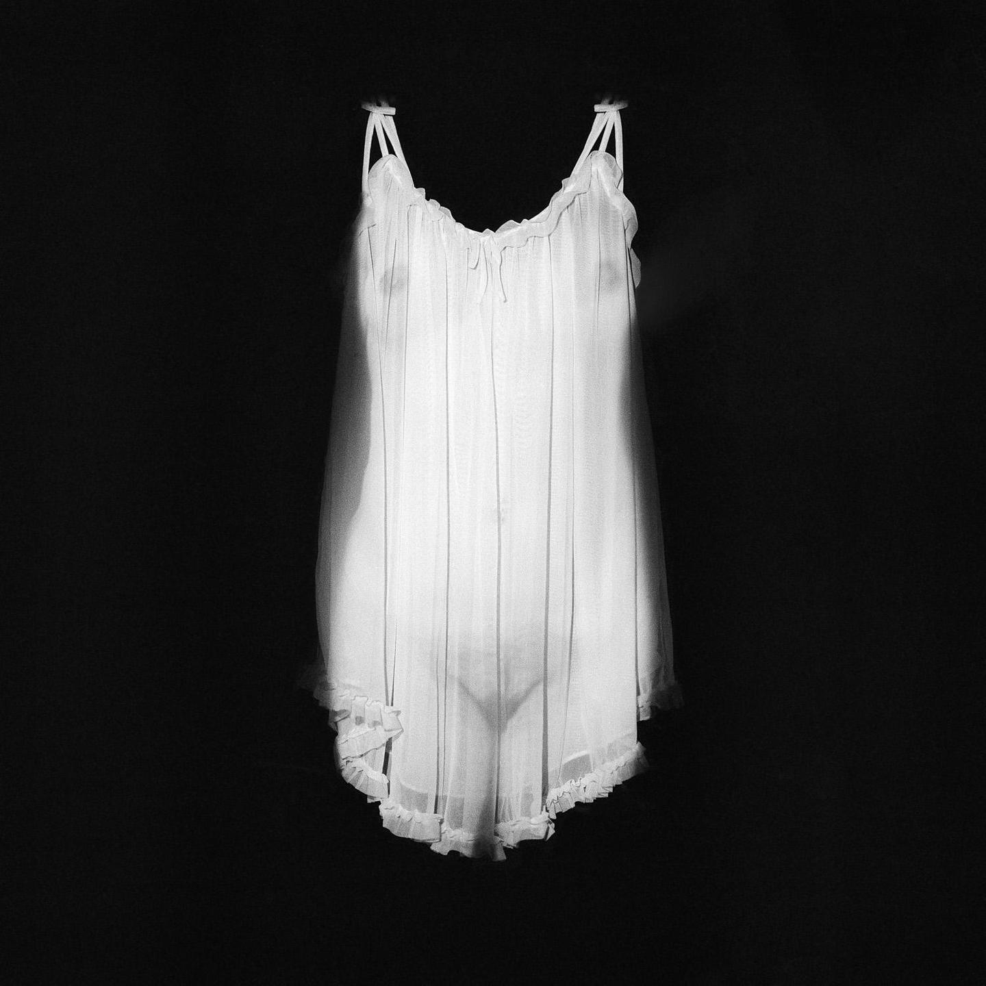 A white nightgown hangs against a dark background, illuminated by a spotlight.