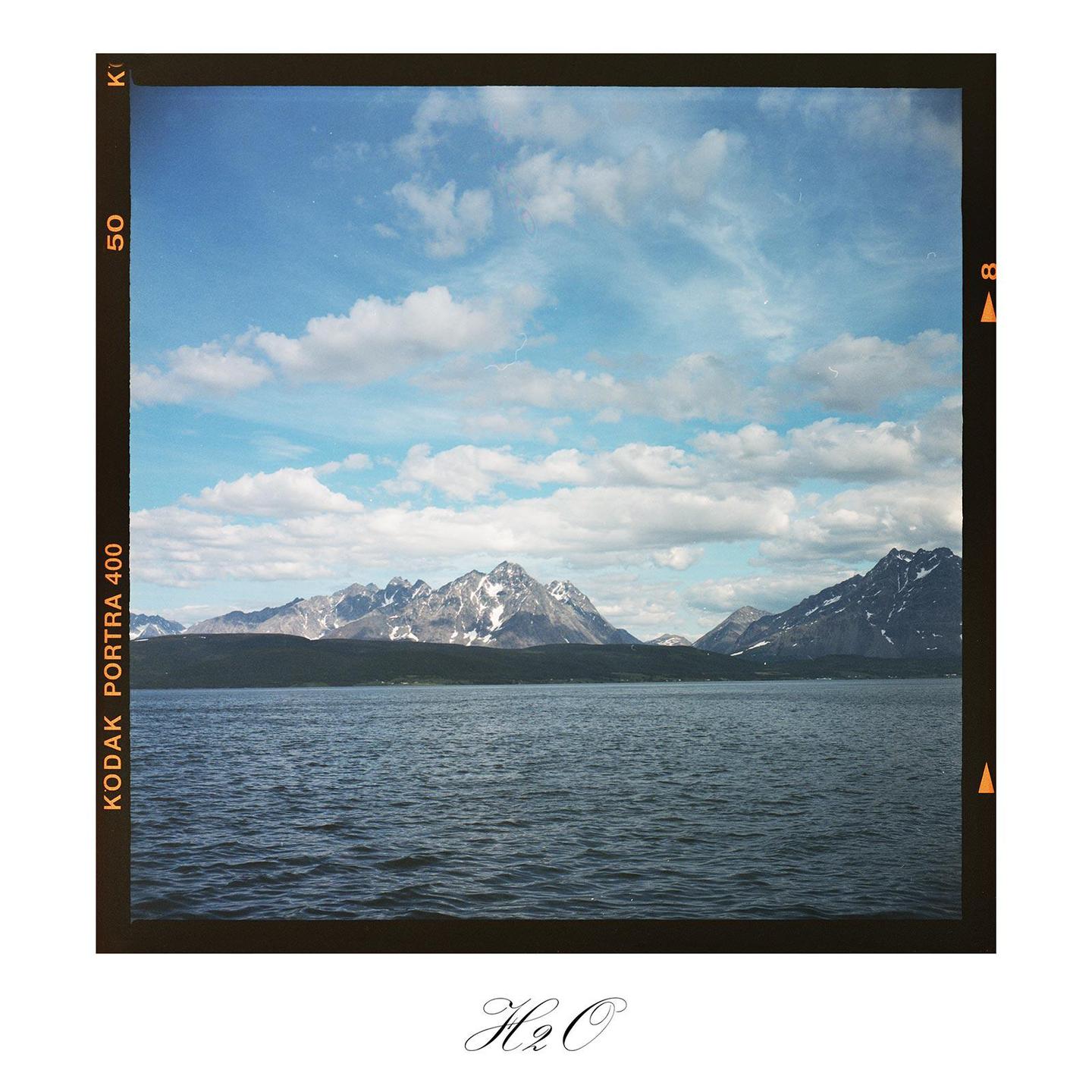 A body of water is in the foreground with snow-capped mountains and a cloudy sky in the background.
