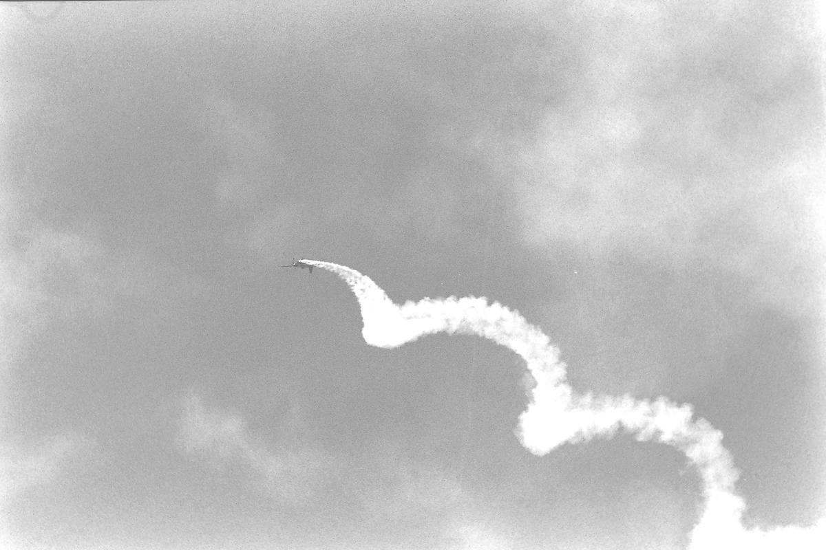 A jet aircraft performs an aerial maneuver, leaving a trail of smoke against a cloudy sky.