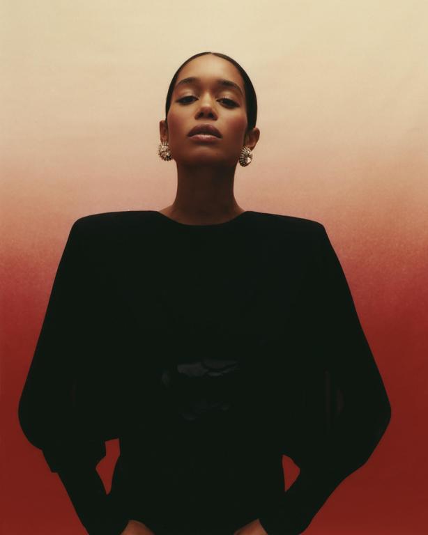 A woman with slicked-back hair and large earrings looks directly at the viewer.