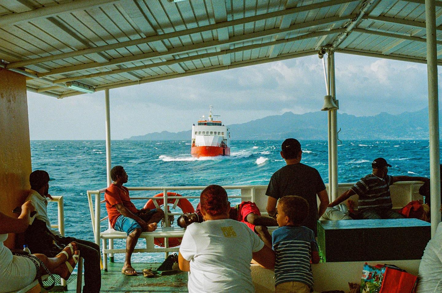 People are riding on a ferry with a view of another ferry and mountains in the distance.