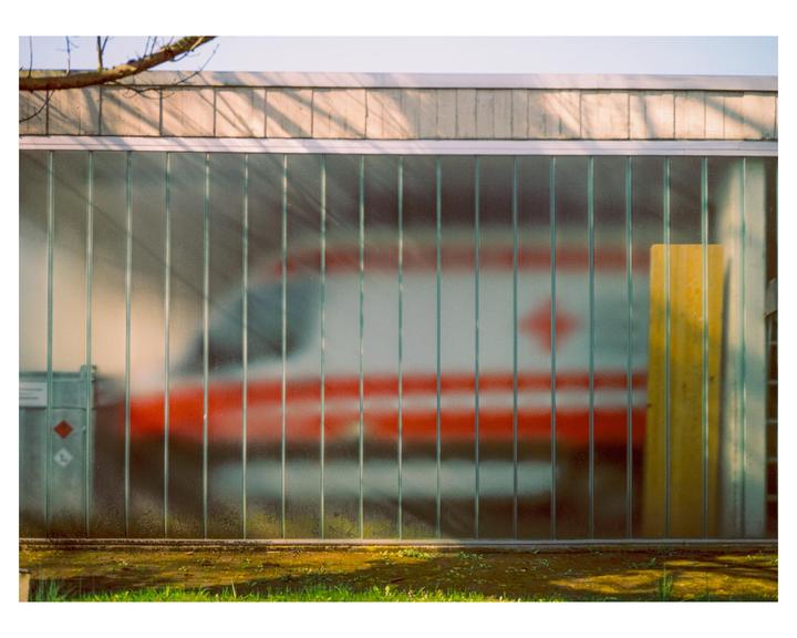 A blurry red and white vehicle is visible behind a glass block wall with green grass in the foreground.