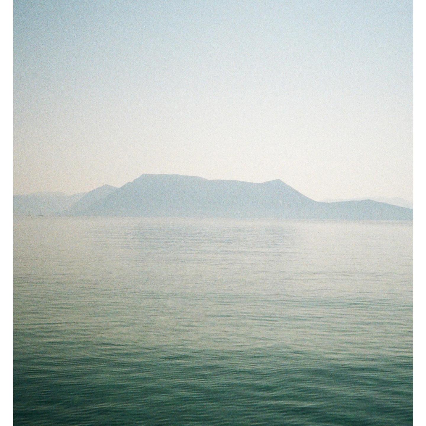 A hazy mountain range rises above a calm body of water.