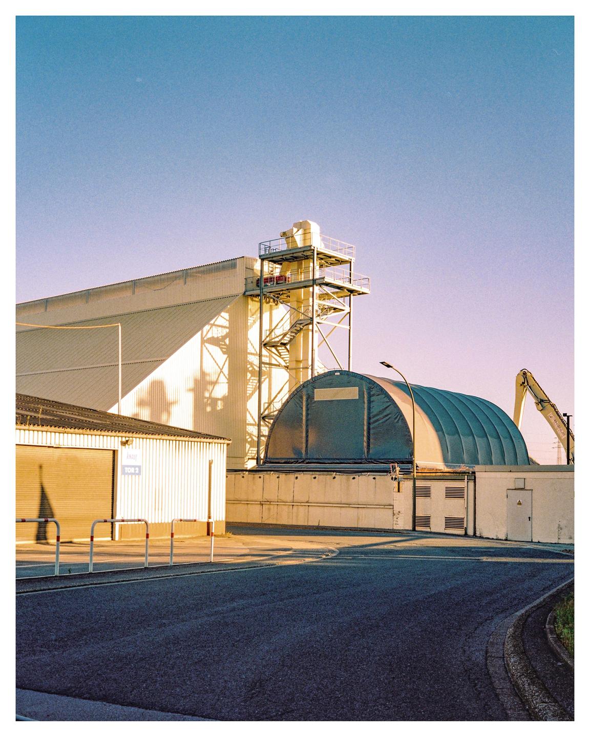 A road curves past industrial buildings under a clear sky.