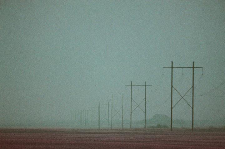 A line of power lines stretches into the hazy distance over a field.