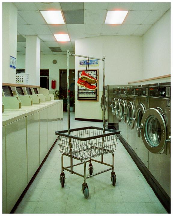 A pair of red sneakers hangs from a laundry cart in a laundromat.