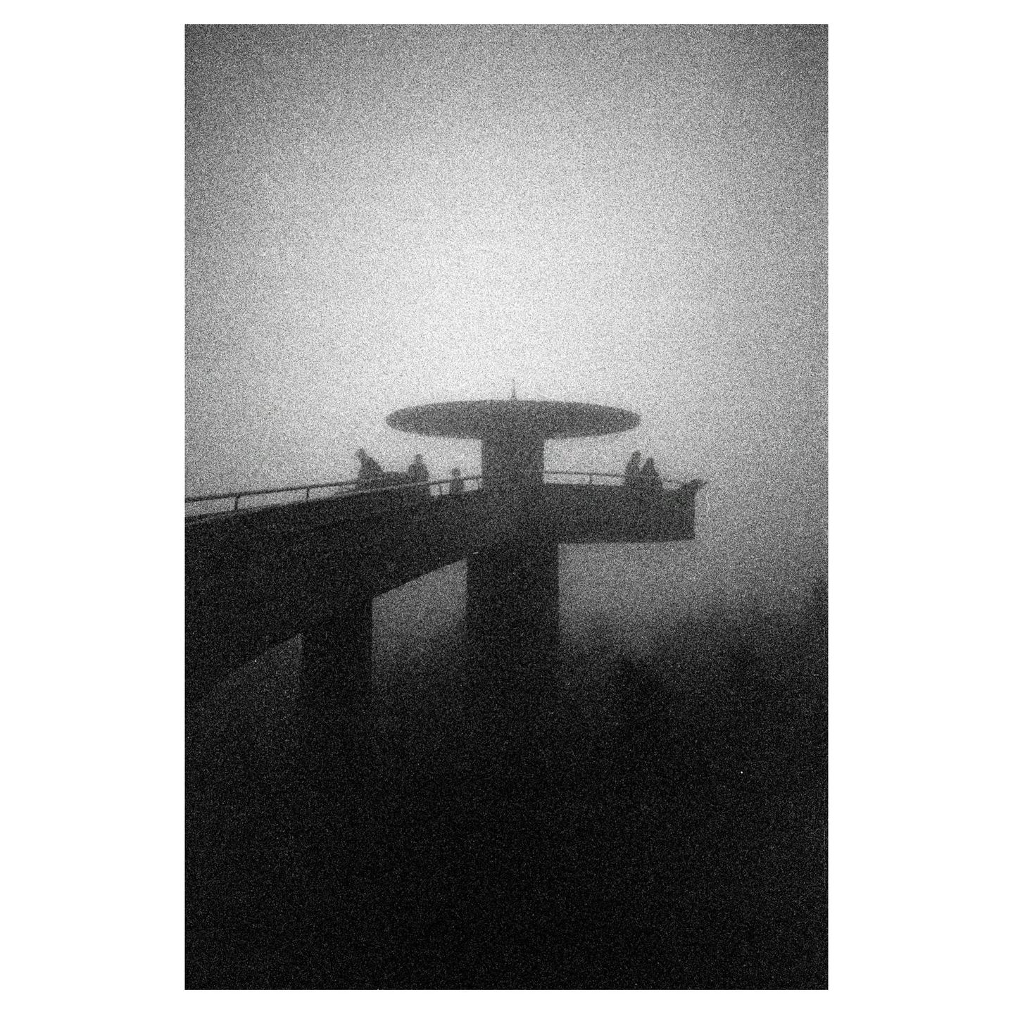 A silhouetted observation tower with people on its platform is shrouded in fog.