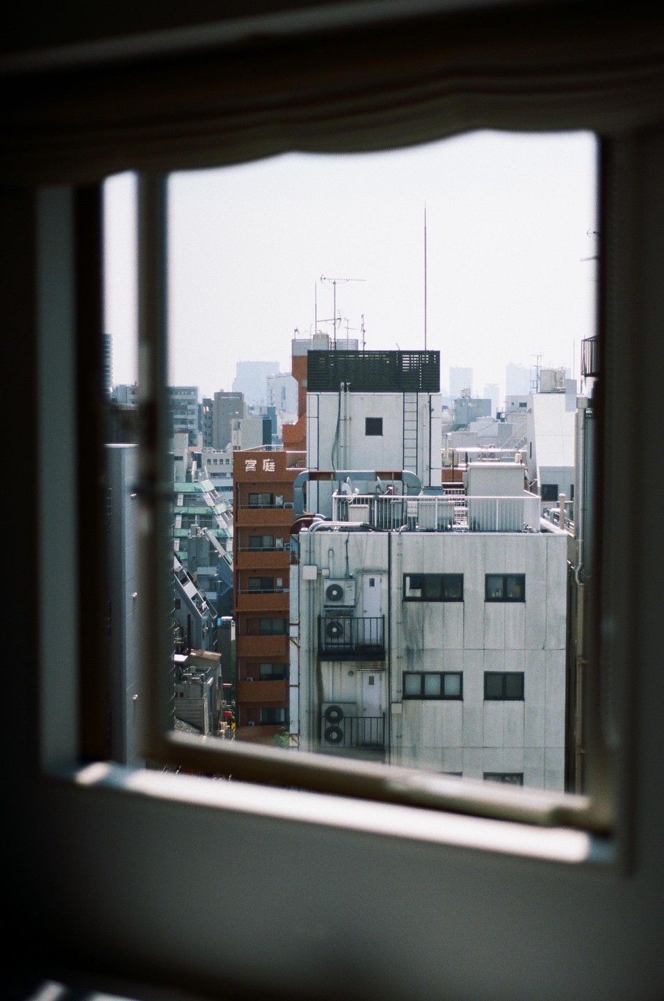A view of city buildings with many air conditioning units and antennas, framed by a window.
