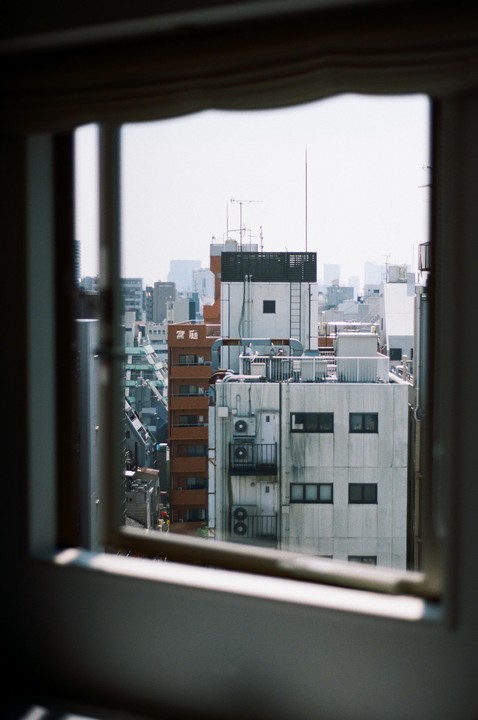 A view of city buildings with many air conditioning units and antennas, framed by a window.