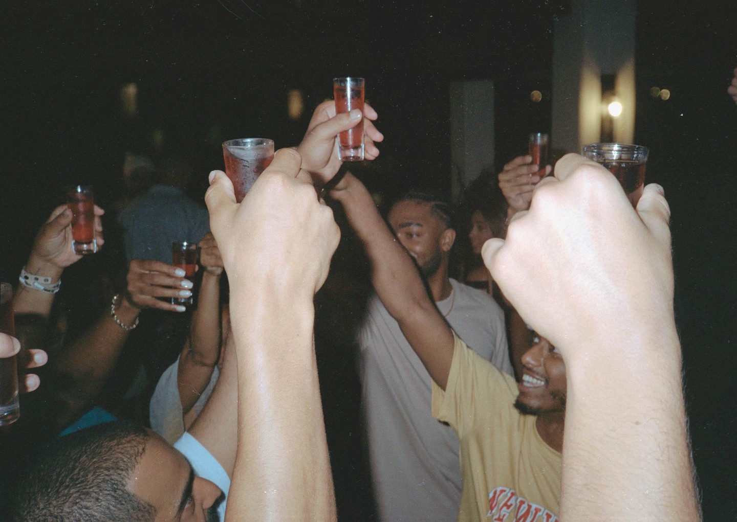 A group of people are holding up shot glasses in a toast at night.