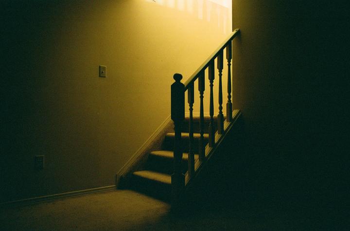 A staircase with a wooden banister leads upwards, illuminated by a warm light from an unseen source.