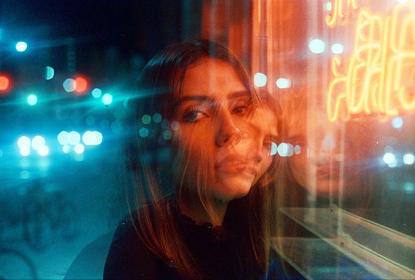 A woman's face is visible through a window with neon lights and streetlights creating a double exposure effect.