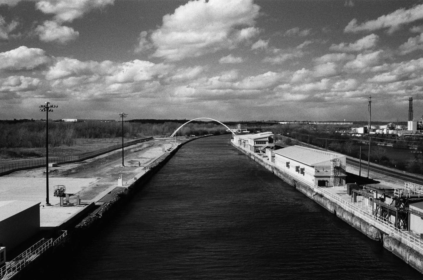 A canal with buildings on both sides leads to an arch bridge under a cloudy sky.