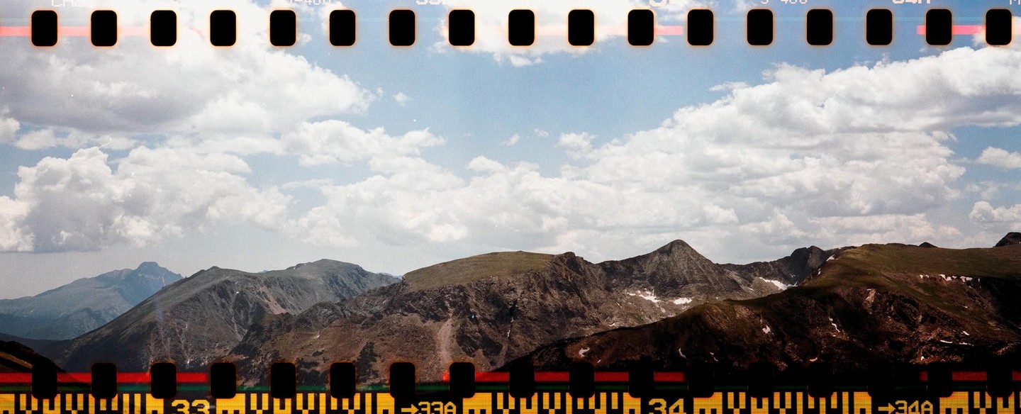 A panoramic landscape shows mountains with patches of snow under a cloudy sky, with film sprockets visible at the top and bottom.