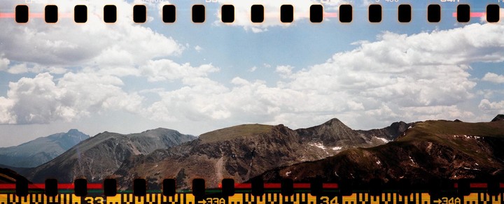 A panoramic landscape shows mountains with patches of snow under a cloudy sky, with film sprockets visible at the top and bottom.