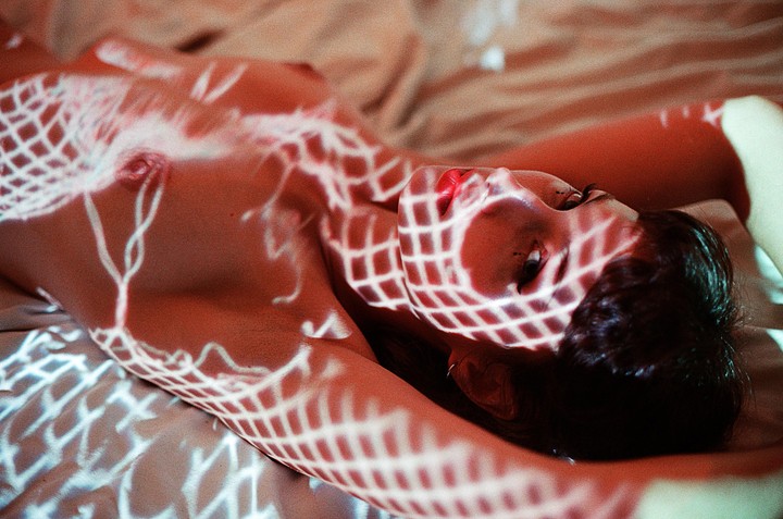 A woman lies on a bed with a grid pattern of light projected onto her body.
