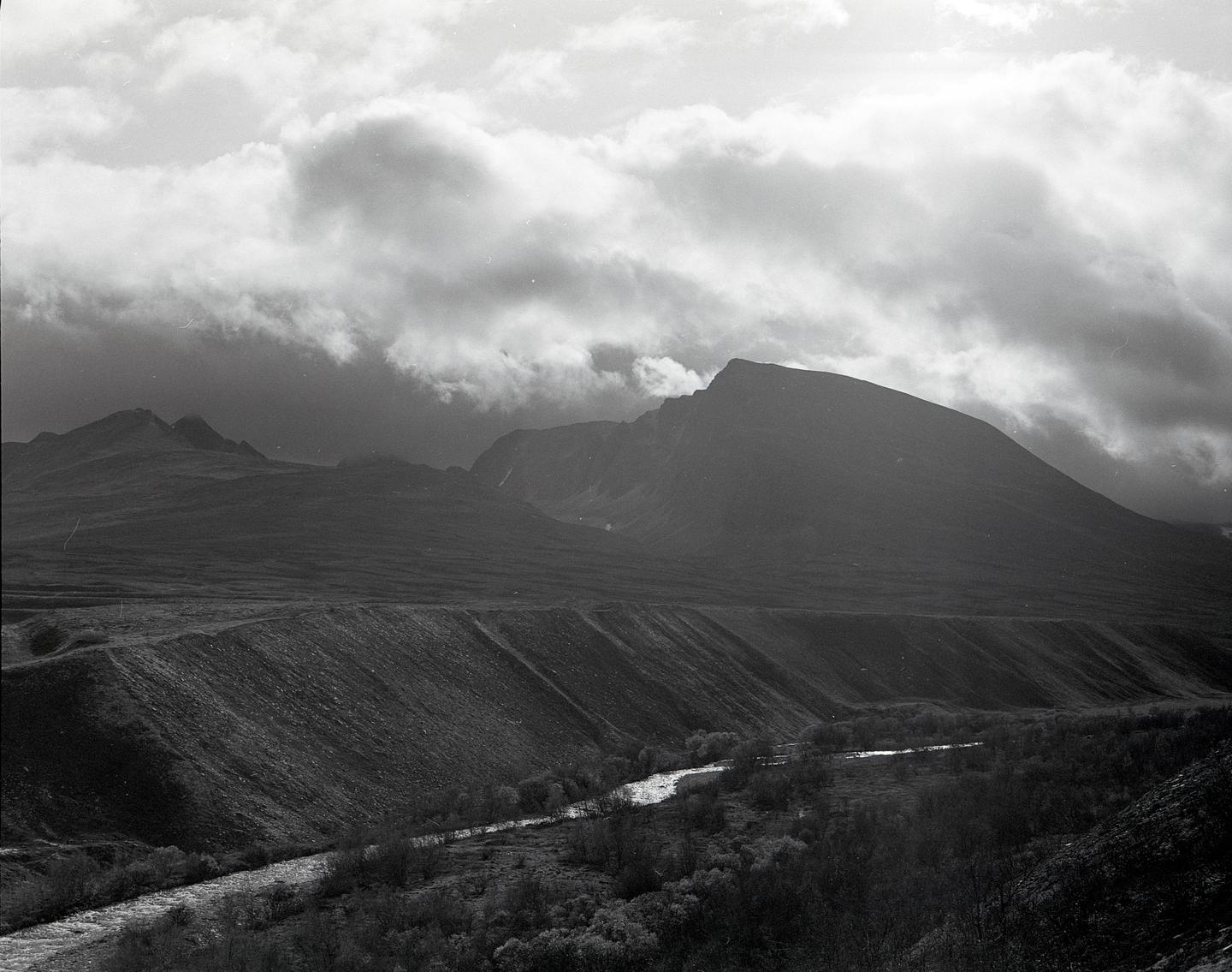 A river flows through a valley with mountains under a cloudy sky.