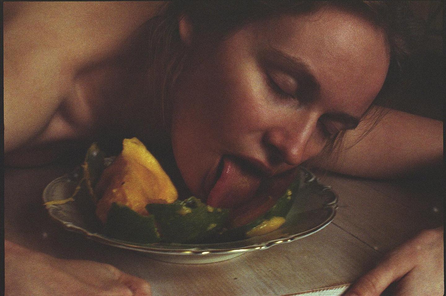 A woman with her eyes closed is licking fruit from a plate.