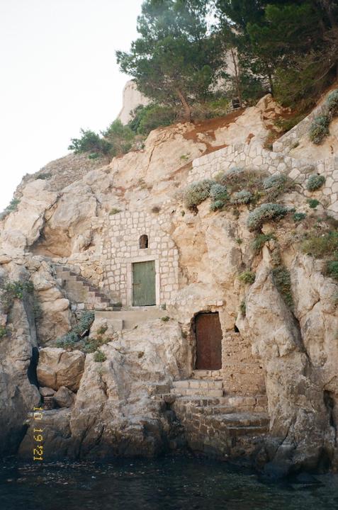 Two doors are built into a rocky cliffside above the water, with a stone staircase leading up to the top of the cliff.