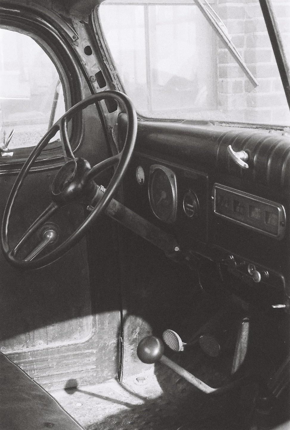 The interior of an old vehicle shows the steering wheel, dashboard, and pedals.