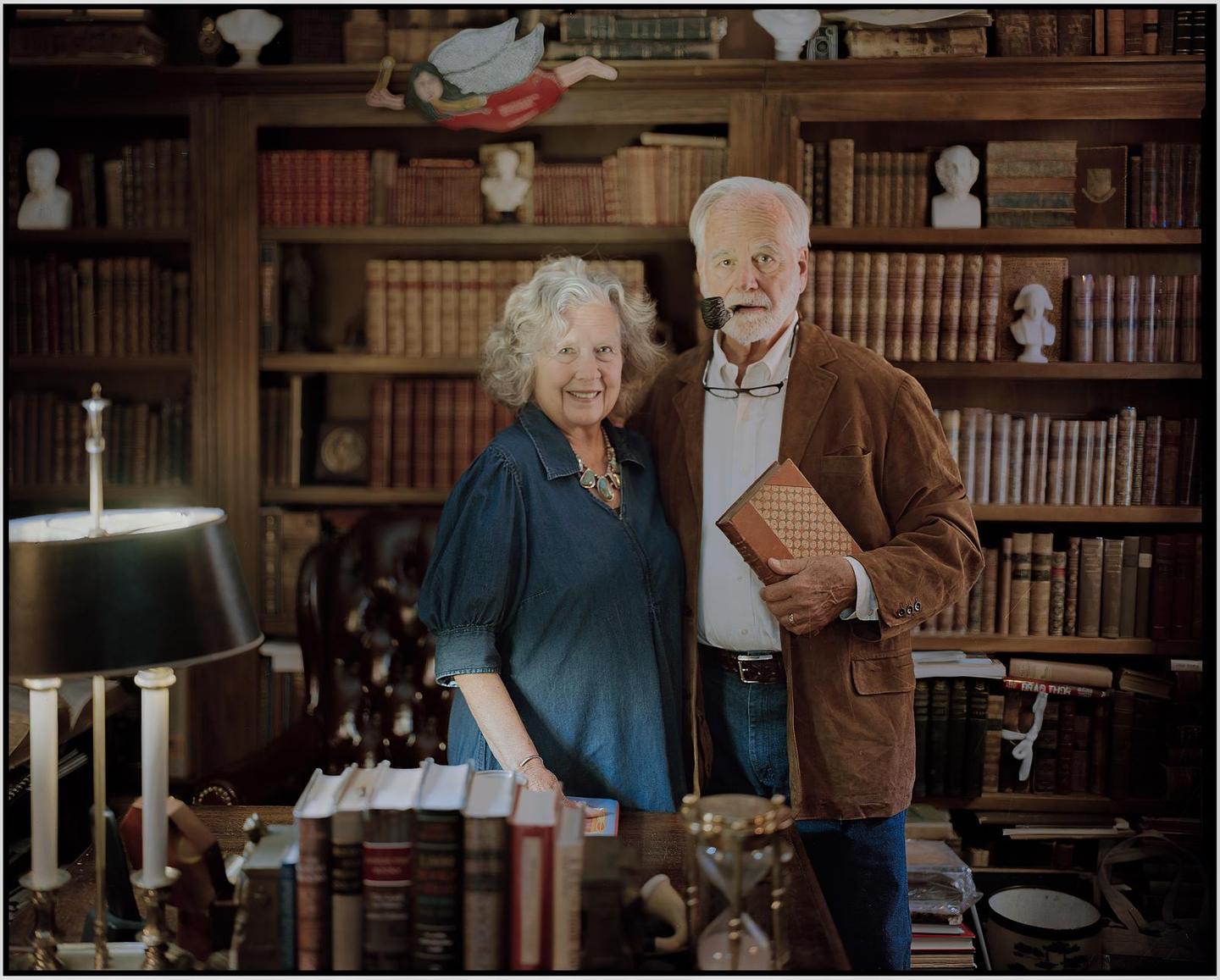 A couple stands in a room filled with bookshelves and books.