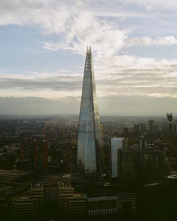 The Shard skyscraper stands tall over the city of London under a cloudy sky.