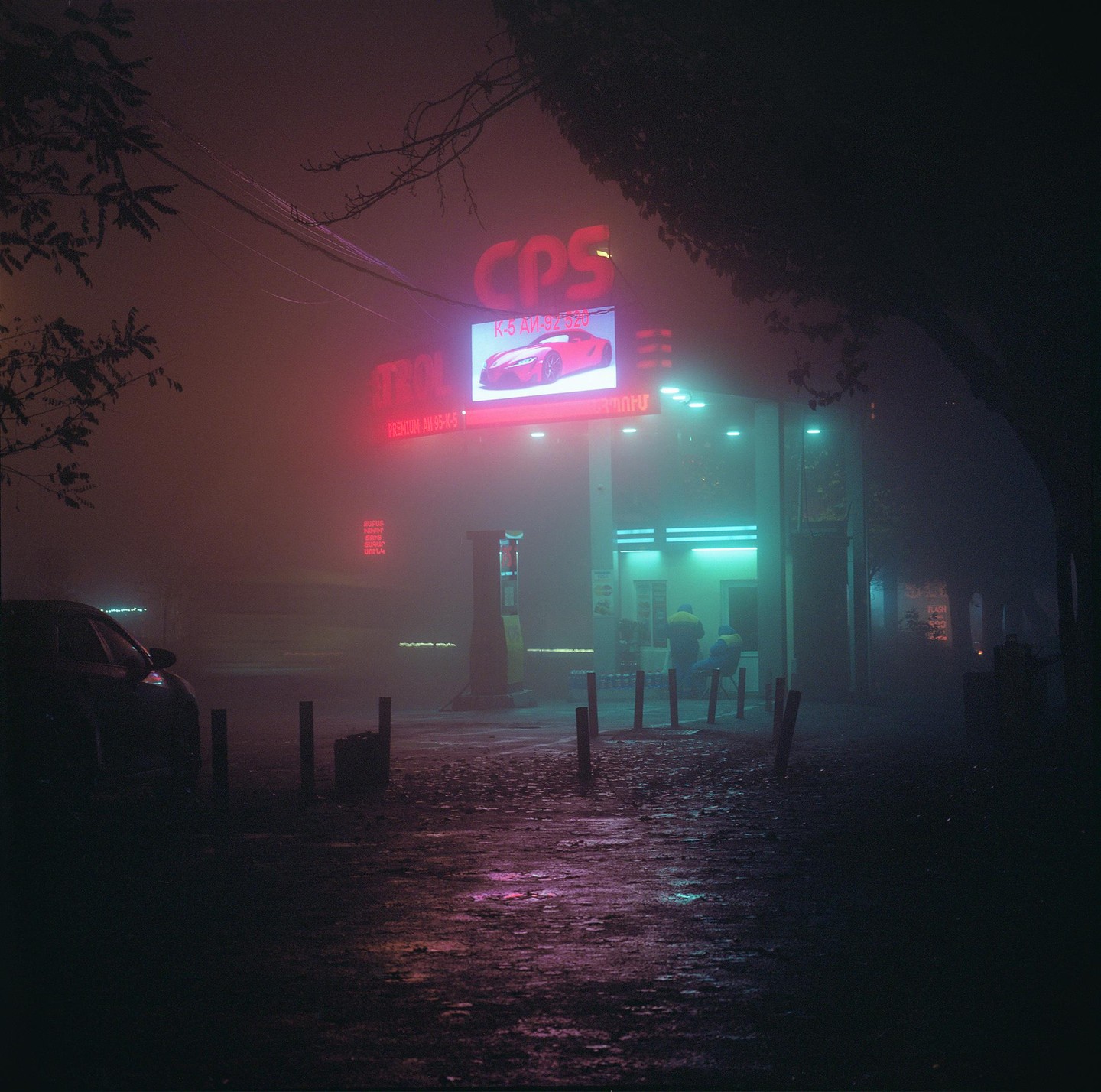 A gas station with neon signs is visible through a thick fog at night.