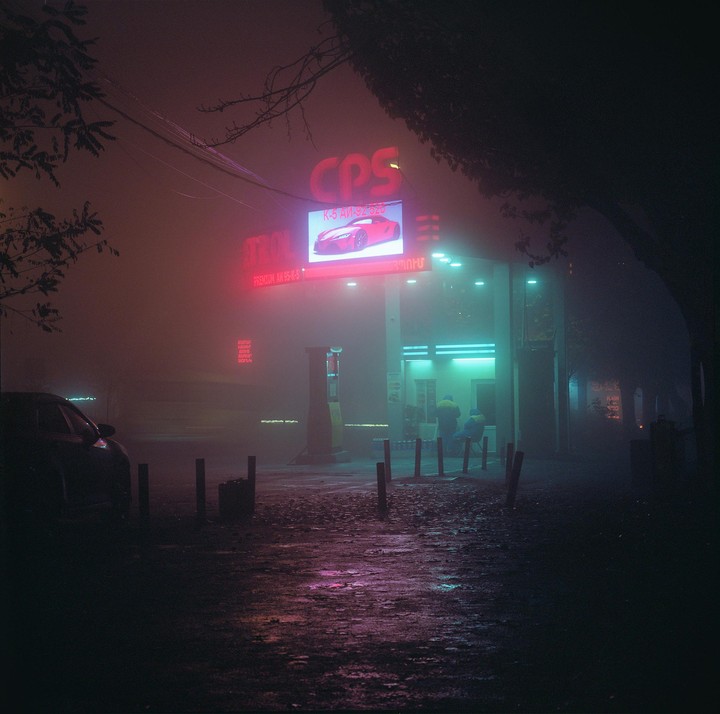 A gas station with neon signs is visible through a thick fog at night.