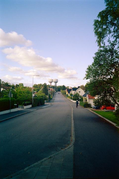 A person rides a bicycle down a residential street with two water towers in the distance.