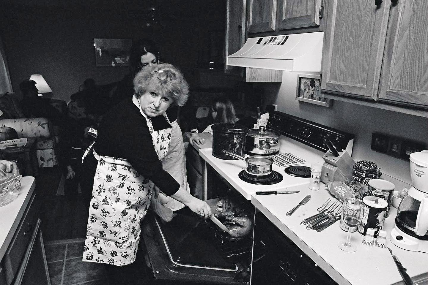 A woman wearing an apron is taking a turkey out of an oven in a kitchen.