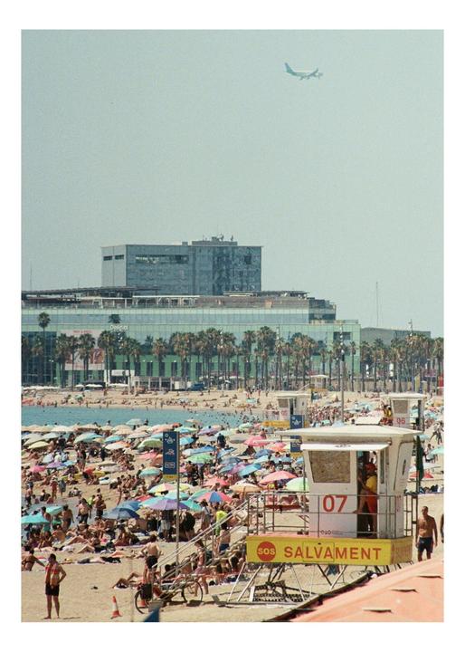 A crowded beach with many colorful umbrellas and a lifeguard tower is visible, with a large building and palm trees in the background and an airplane flying overhead.