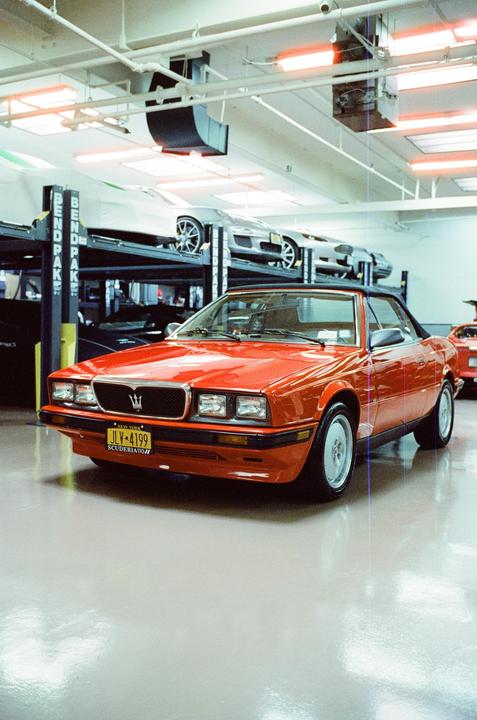 A red convertible car is parked in a garage with other cars on lifts in the background.